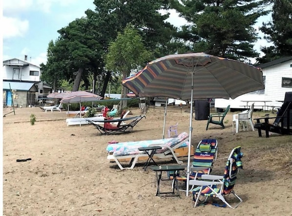 Un espace extérieur sablonneux aménagé avec des chaises de plage, des parasols et un petit lit.