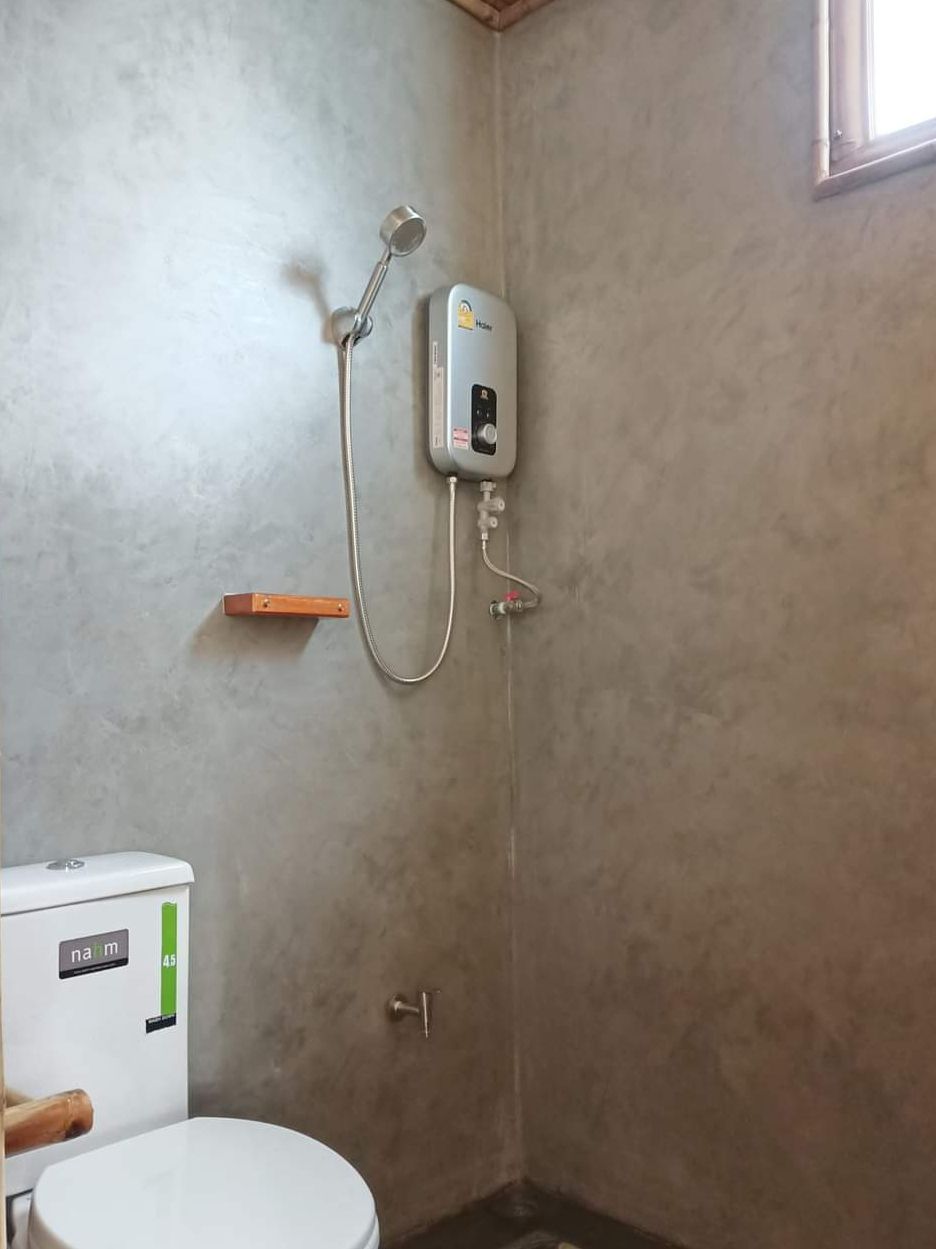 A bathroom with a toilet, a shower unit, and a wall-mounted shelf.