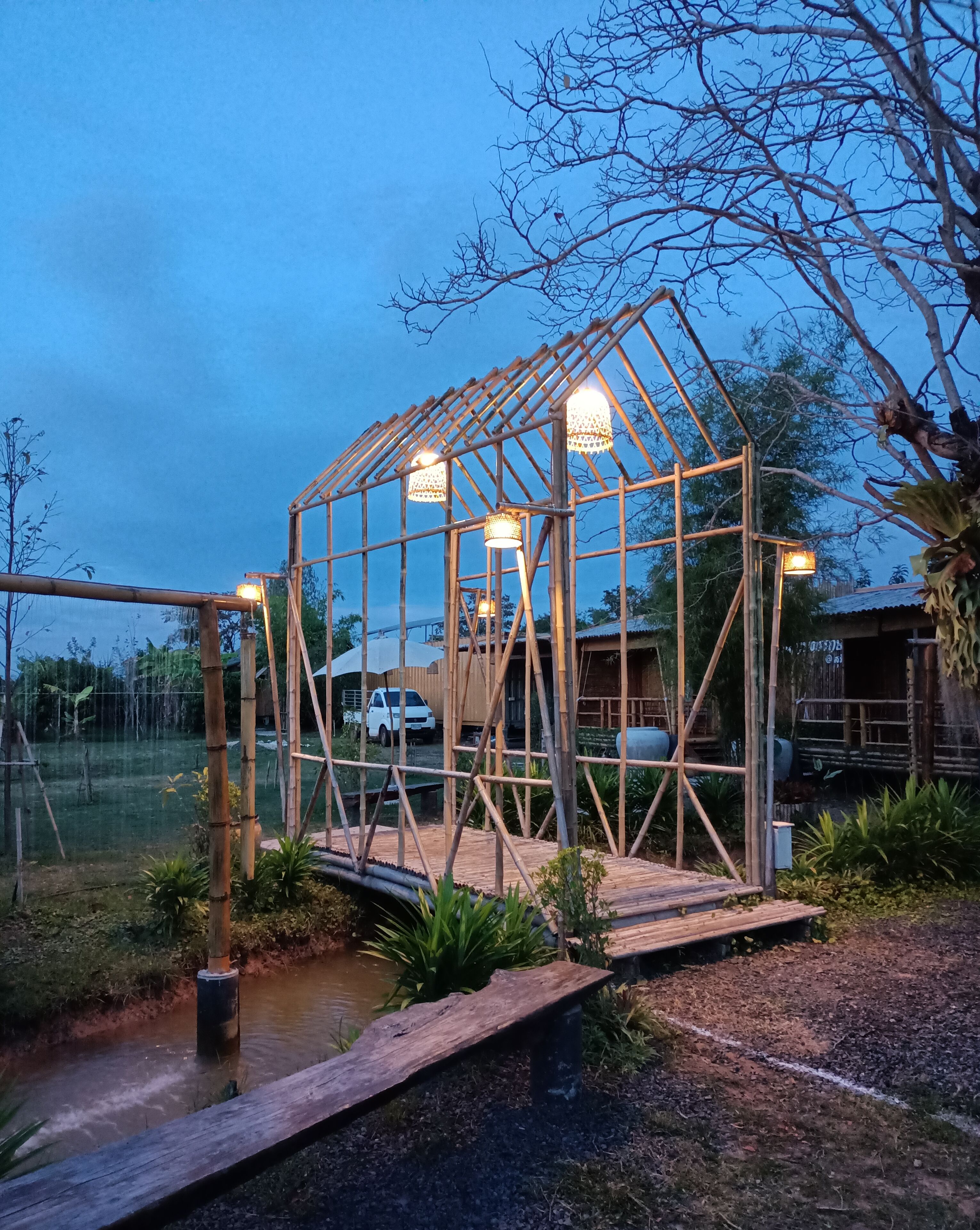 Een houten constructie met een dak, omgeven door planten en een klein waterpartij.