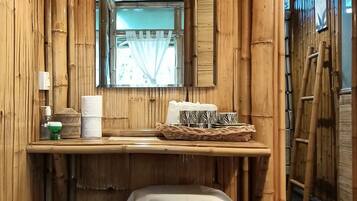 A room with bamboo walls, a wooden table with a white tablecloth, a wicker basket, a stool, and a hanging light fixture.