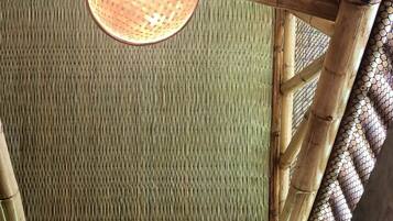 A bamboo-framed room with a woven ceiling light, a shower area, and a water heater.