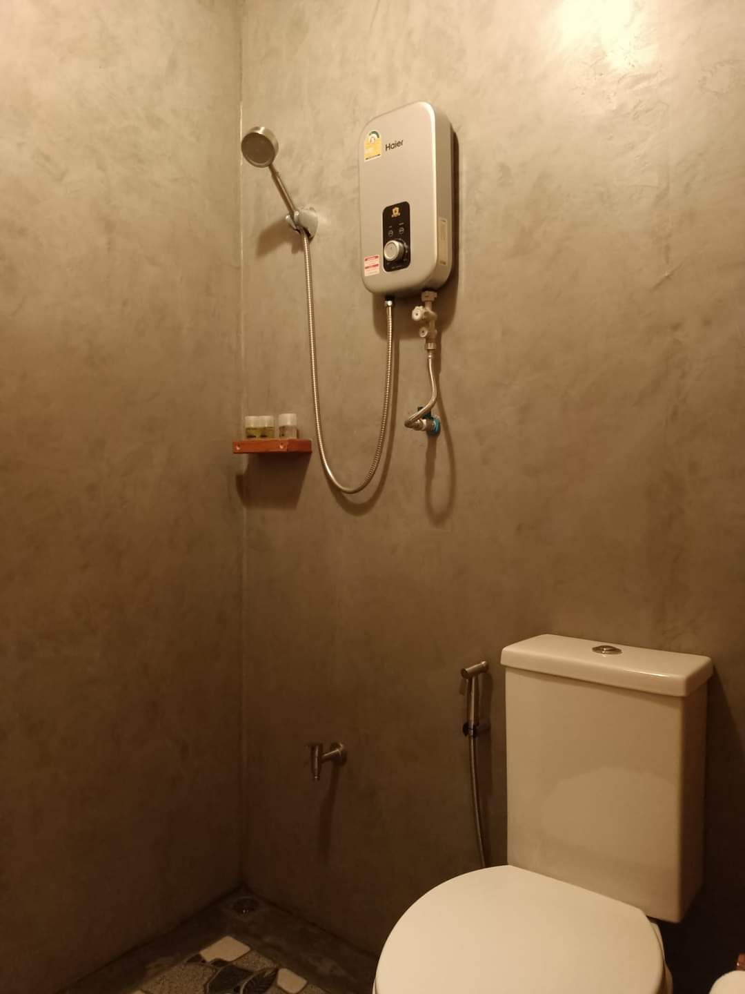Une petite salle de bain comprenant des toilettes, une douche et une étagère avec des articles de toilette.