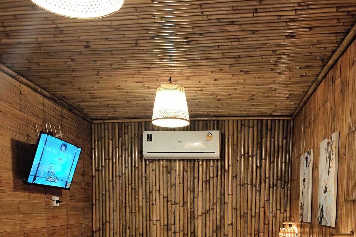 A room with a bed, a TV mounted on the wall, an air conditioning unit, and wooden paneling.