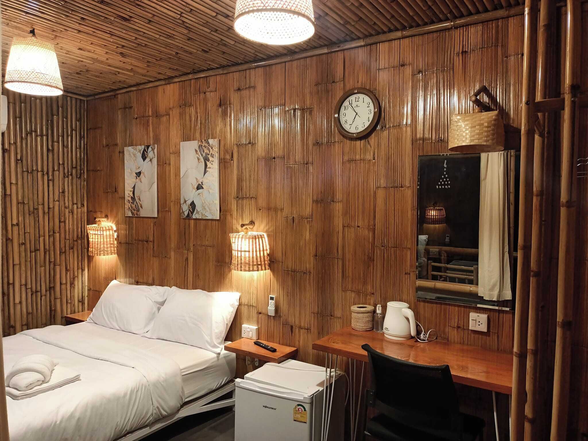 A room with a bed, bedside table, desk, chair, and a clock on the wall.