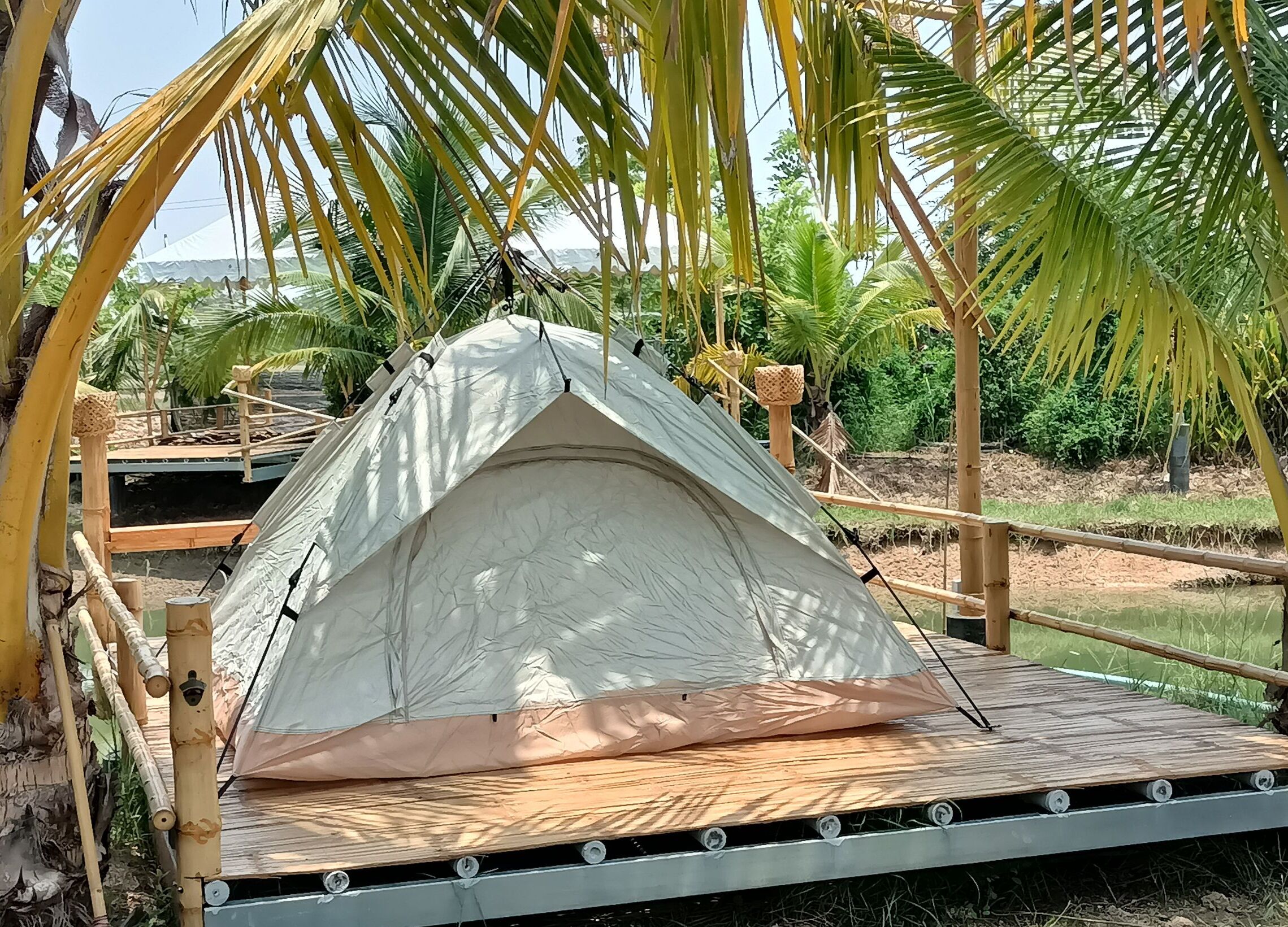 Una tenda bianca su una piattaforma di legno, con un'amaca e pali di bambù.