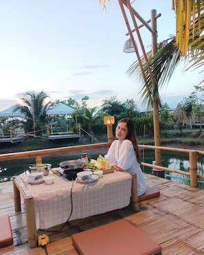 Una persona sentada a una mesa con vista a un cuerpo de agua y vegetación.