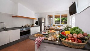 A modern kitchen with a central island, a dining area with a view, and a TV mounted on the wall.