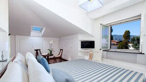 A bedroom with a bed, a TV, a desk, and a window with a view.