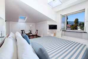 A bedroom with a bed, a TV, a desk, and a window with a view. - AMORE RENTALS - Villa Flavia with Private SPA, Swimming Pool, Terraces, Sea View (Sorrento)