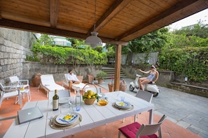 An outdoor patio with a wooden pergola, white lounge chairs, a dining table set with plates, glasses, and a laptop. - AMORE RENTALS - Villa Flavia with Private SPA, Swimming Pool, Terraces, Sea View (Sorrento)