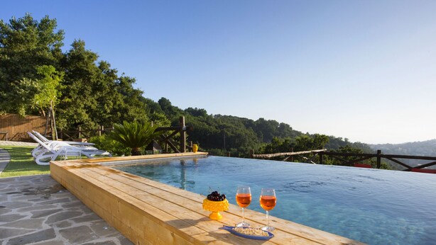 A wooden deck with a pool, two glasses of wine, and a fruit bowl. - AMORE RENTALS - Casa I Giardini di Sorrento with Swimming Pool, Sauna, Sea View (Sorrento)