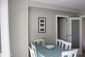 A dining area with a table set for four, chairs, a bowl, a vase, and a framed picture on the wall.