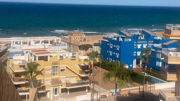 Un hotel costero con varias edificaciones, incluyendo una estructura azul destacada con balcones, vistas a la playa y una zona de piscina.
