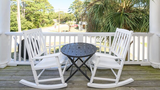 Une terrasse en bois avec une balustrade blanche, deux fauteuils à bascule et une table ronde.