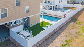 Un bâtiment à deux étages doté d’une cour arrière clôturée, d’une piscine et d’un patio aménagé avec du mobilier d’extérieur.