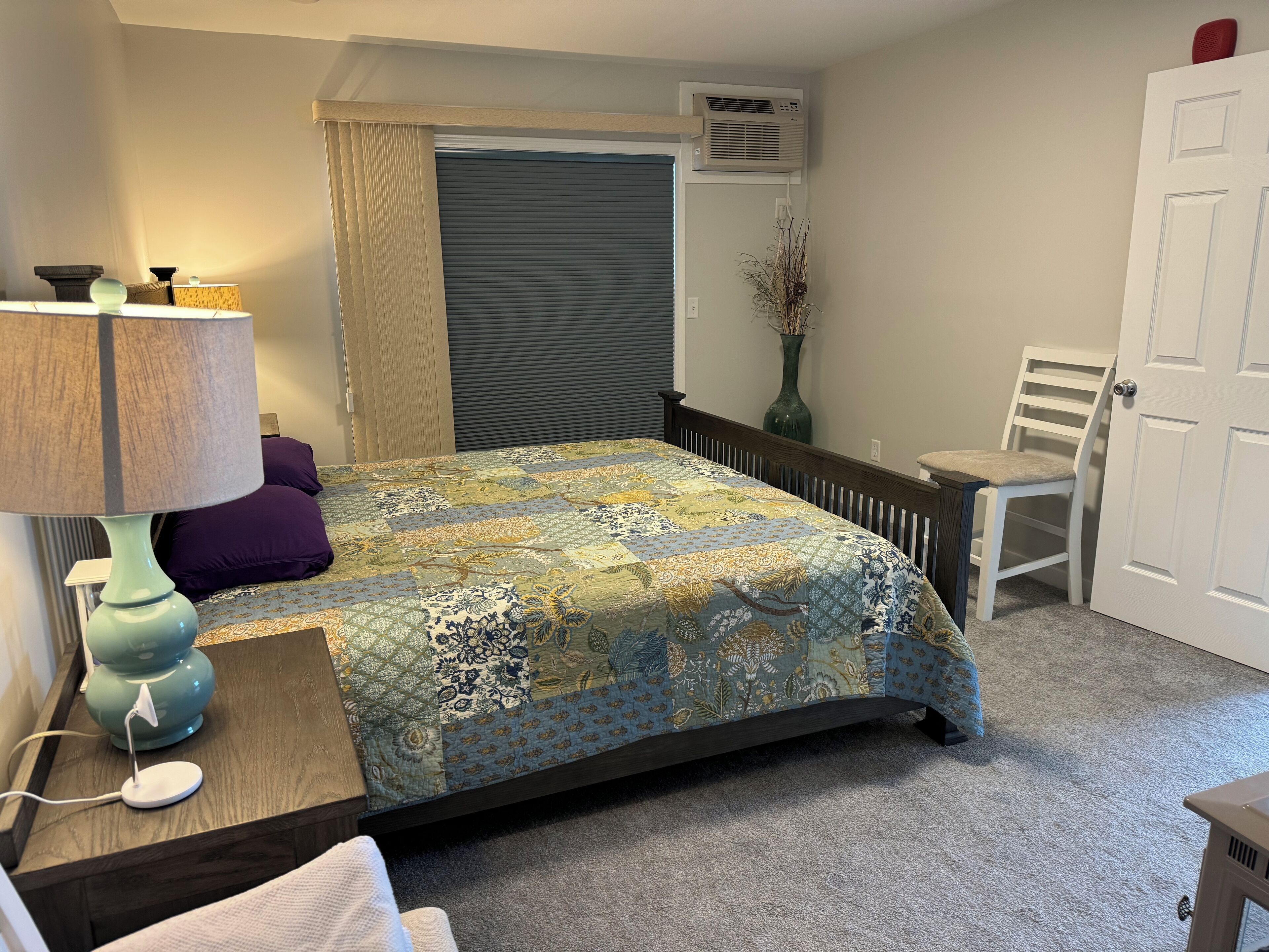 Quarto com cama, luminária, cadeira, vaso e ar condicionado.