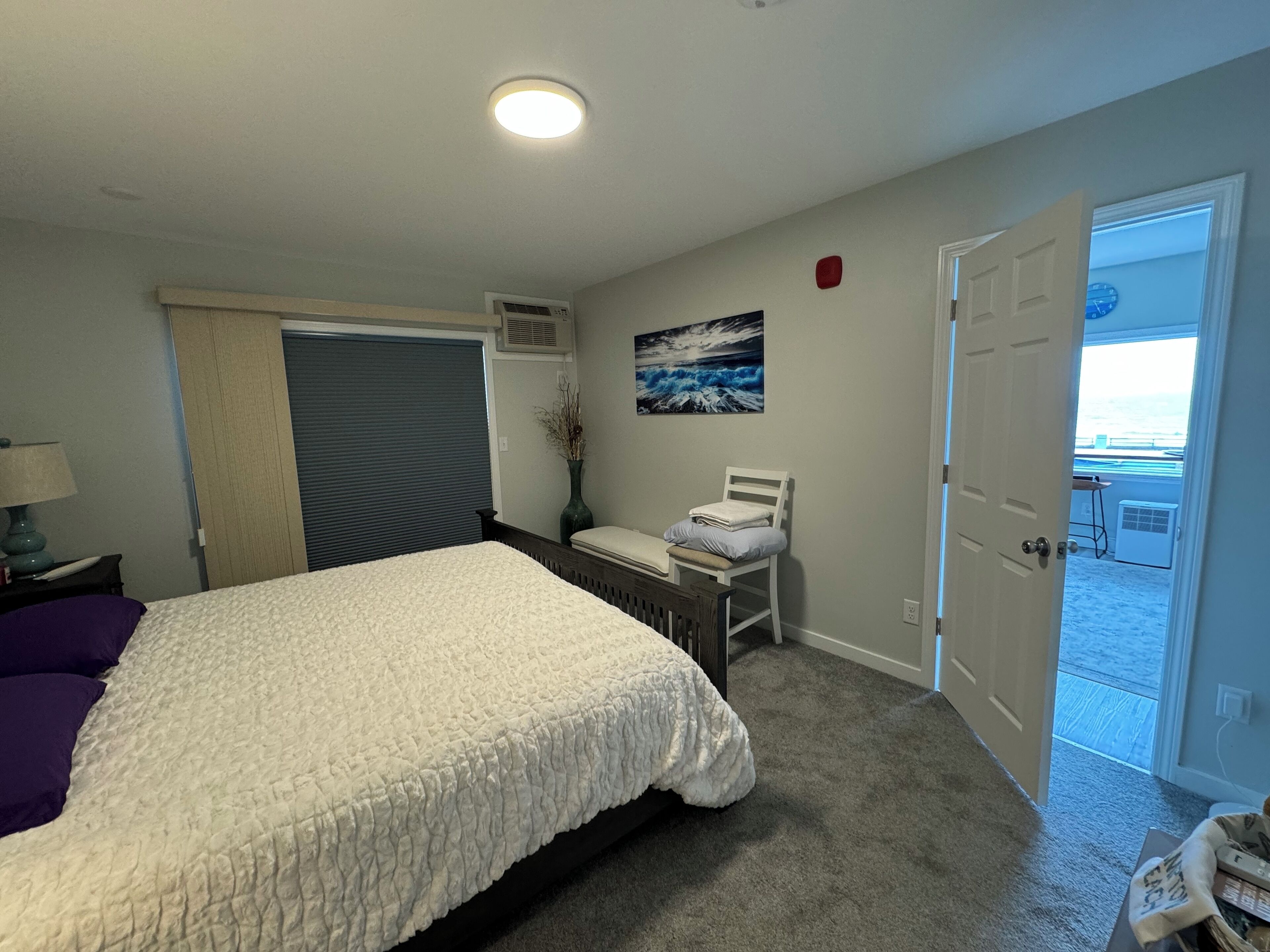 A bedroom with a large bed, a chair, a painting, and a door leading to a balcony.
