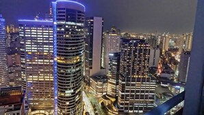 A nighttime cityscape with high-rise buildings, one with a distinctive blue-lit top. - SMDC Air Residences Makati (Makati)