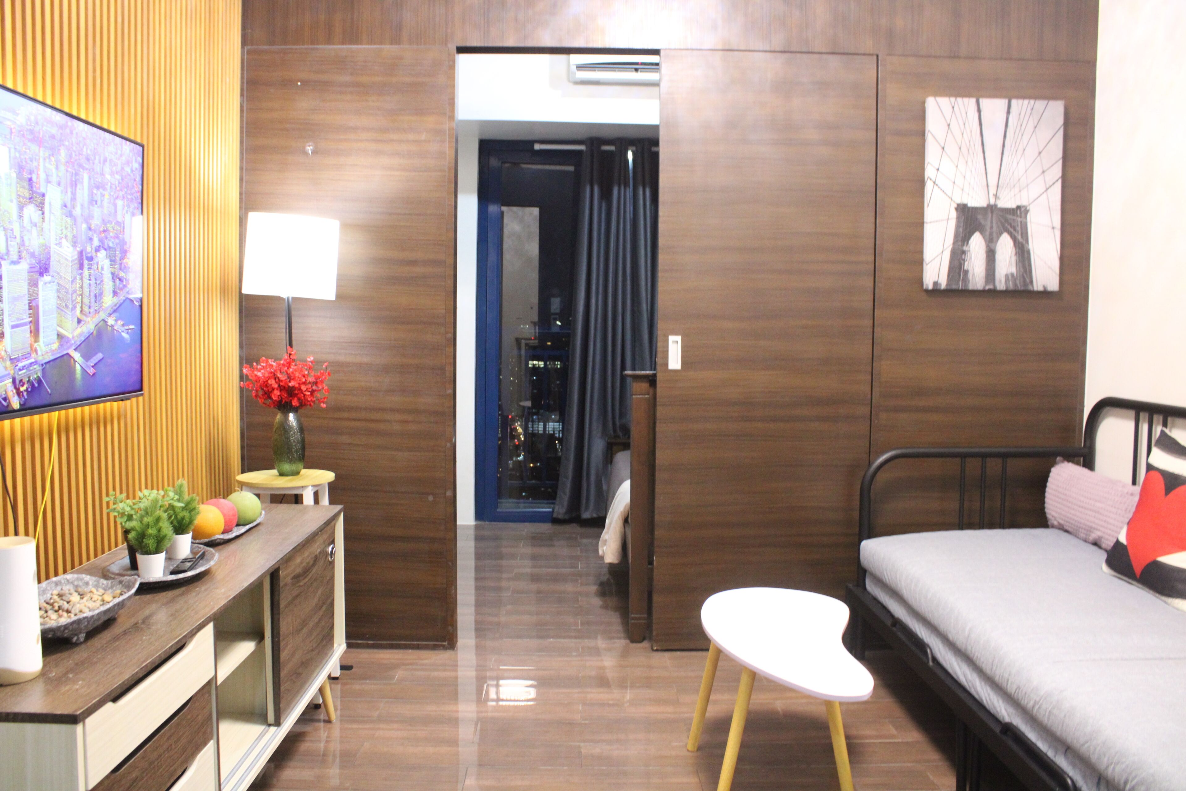 Une chambre d’hôtel moderne, équipée d’un lit, d’une télévision, d’une petite table avec une lampe, et offrant une vue sur le paysage urbain par la fenêtre.
