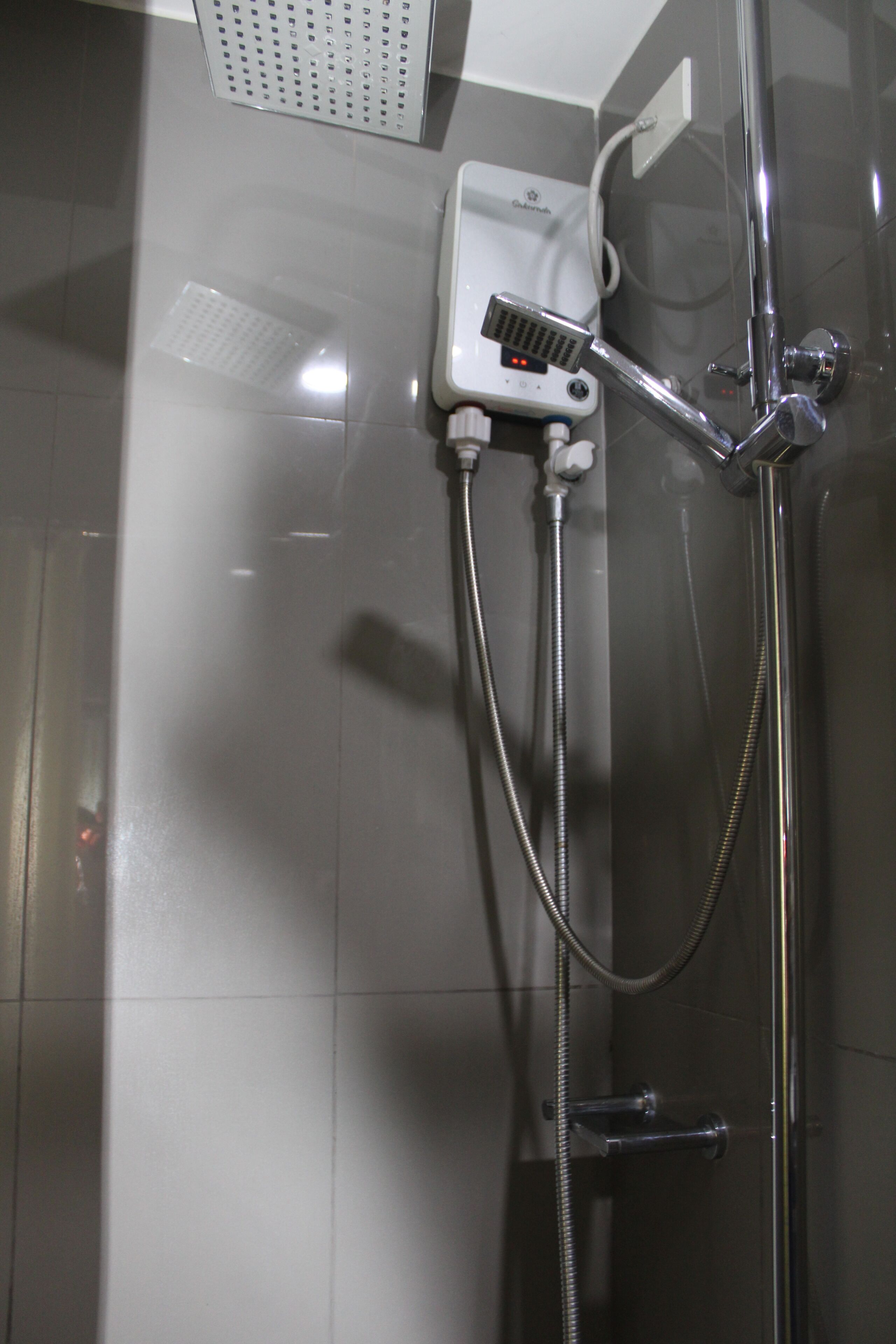 A shower with a handheld showerhead, a wall-mounted control panel, and a flexible hose.