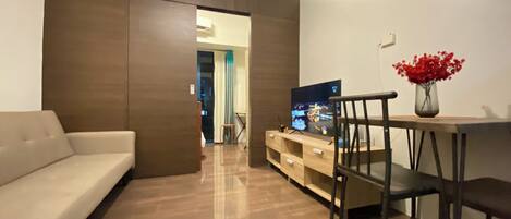 Una sala de estar moderna con un sofá, un televisor sobre un mueble de madera y un jarrón con flores rojas.