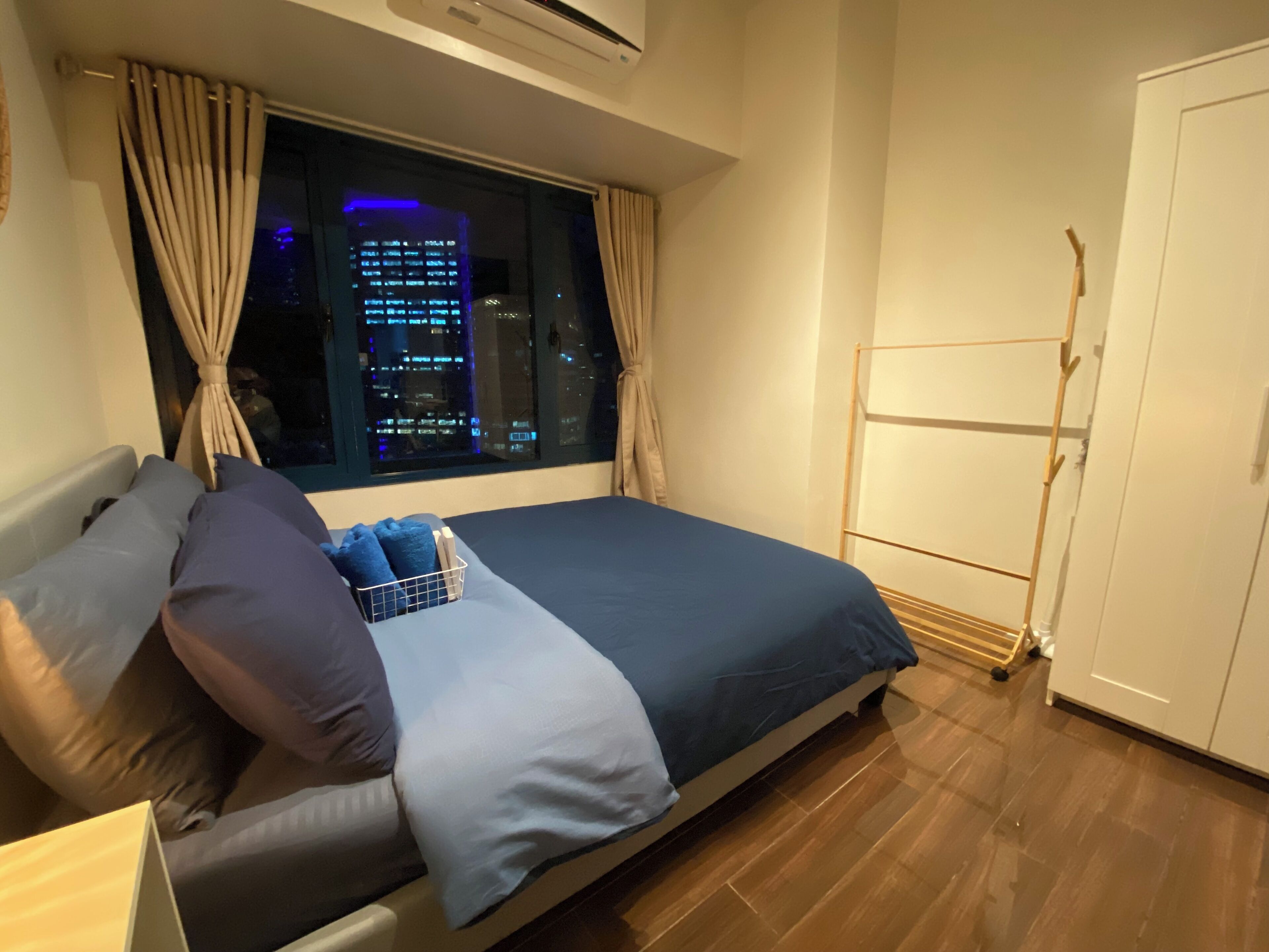 Een slaapkamer met een bed, een raam met gordijnen, een houten vloer en een kledingkast.