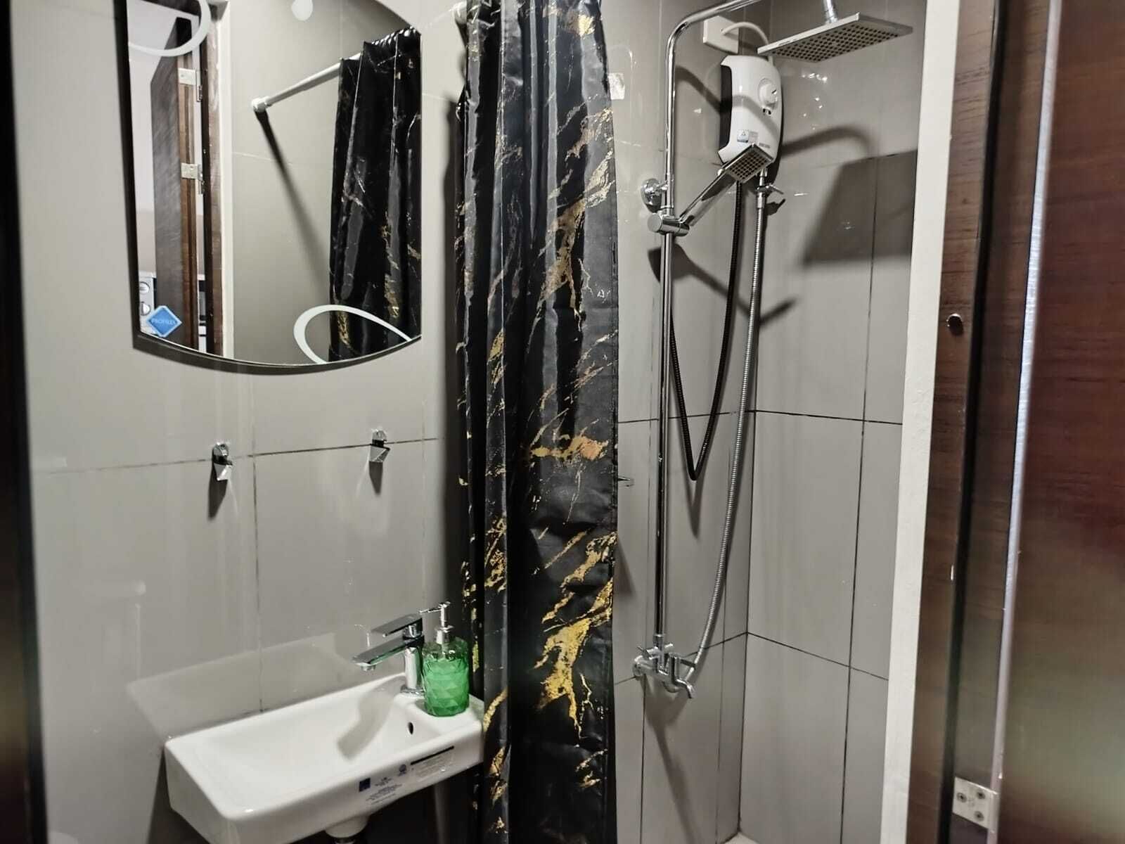 A bathroom with a white sink, a mirror, a shower with a handheld showerhead, and a black and gold shower curtain.