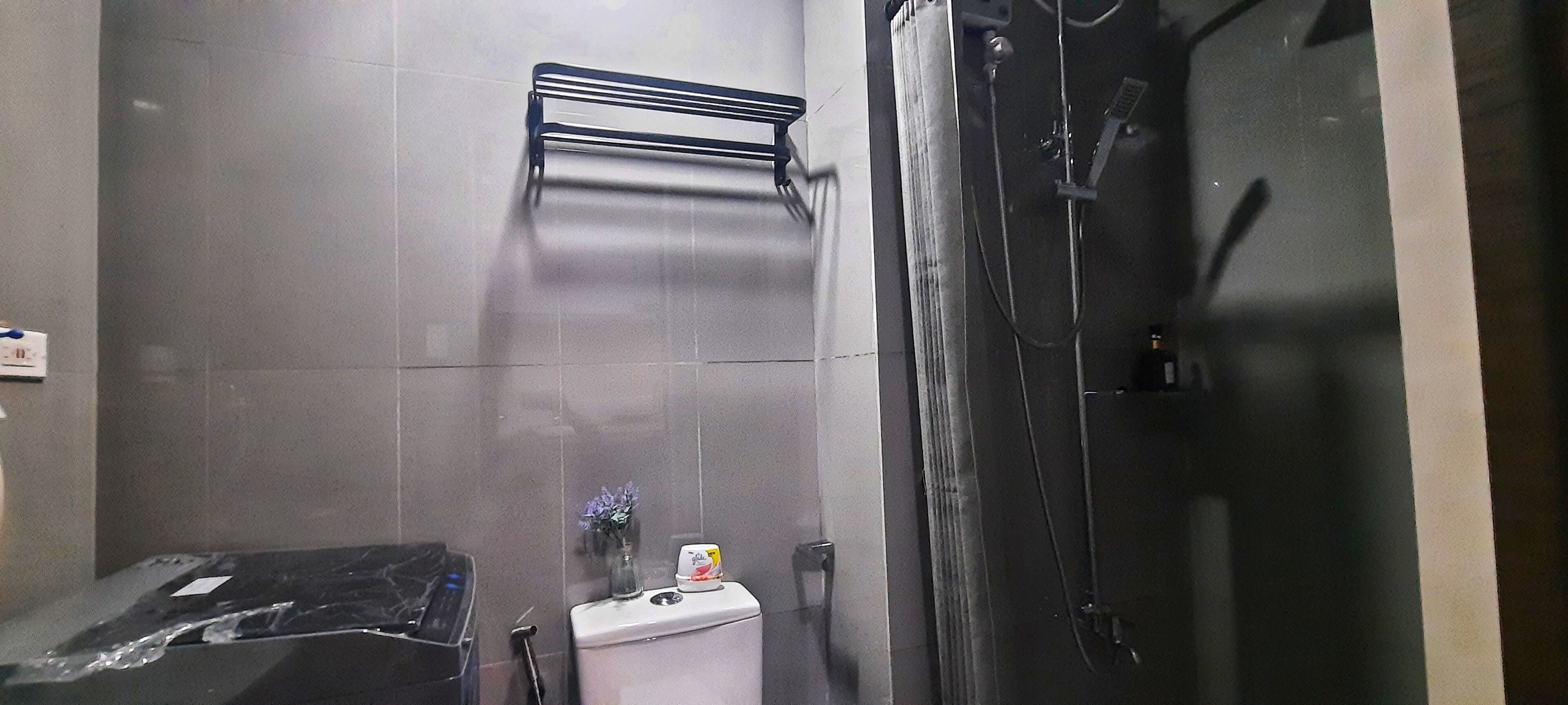 A bathroom with a shower, a towel rack, a toilet, and a small vase with flowers.