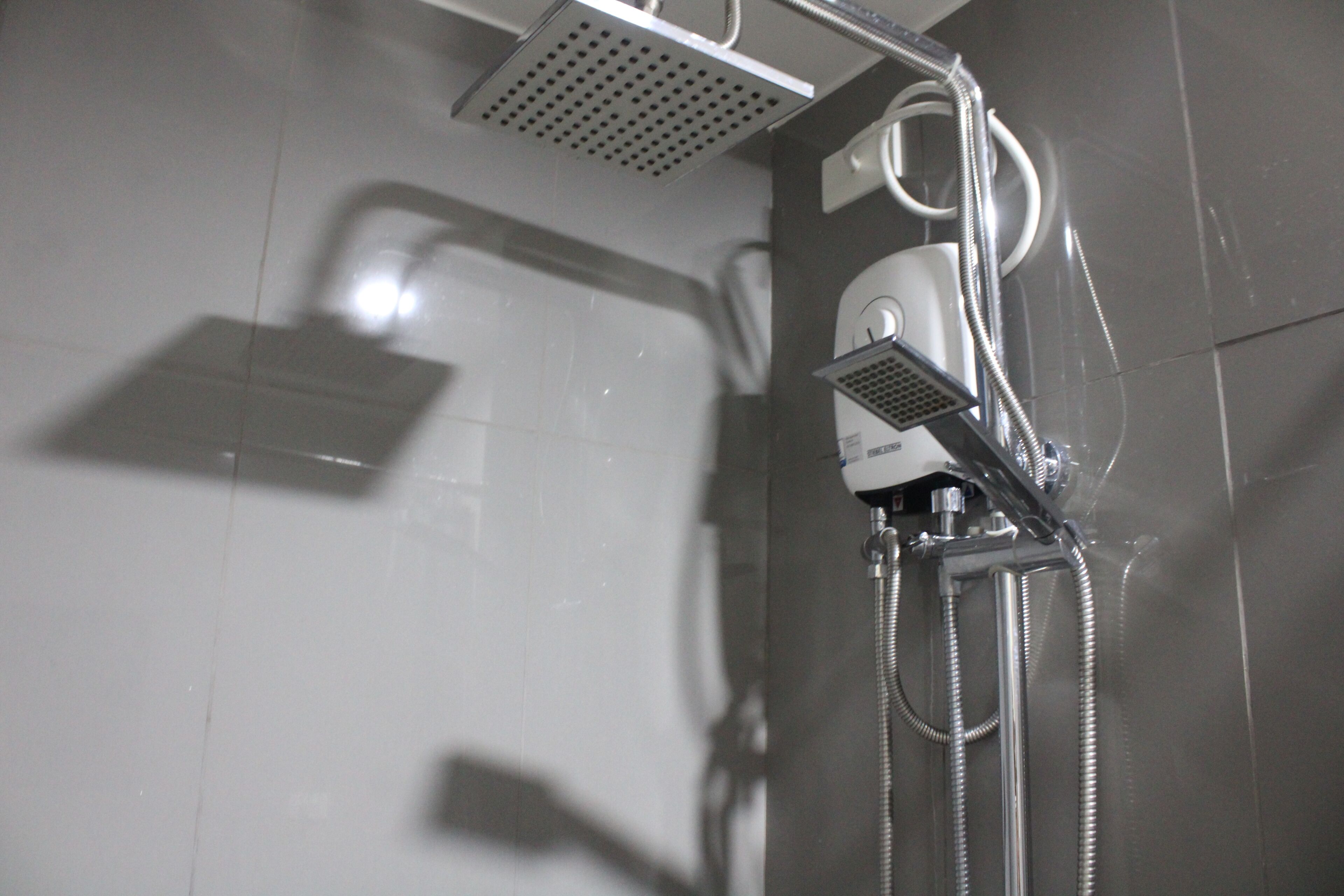 A shower with a handheld showerhead, a wall-mounted control panel, and a flexible hose.