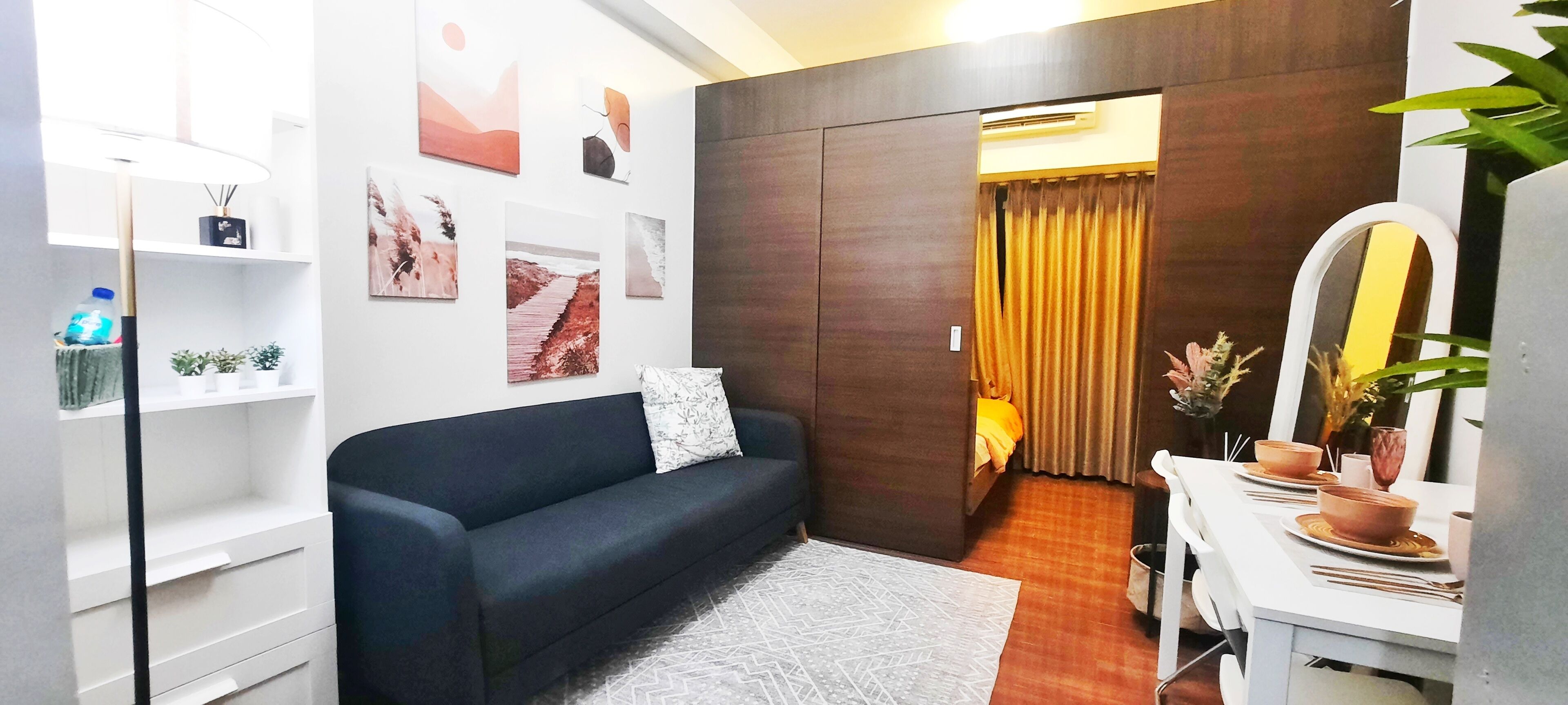 Une chambre d’hôtel moderne avec un canapé bleu foncé, un bureau blanc doté d’un miroir et un coin repas avec une table mise pour deux personnes.