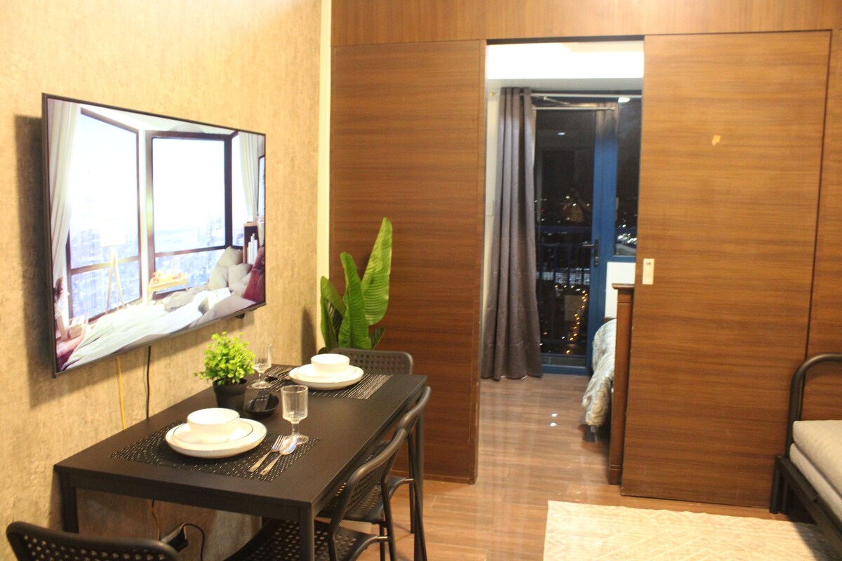 A hotel room with a dining area, a bed, a TV, and a view of the city.