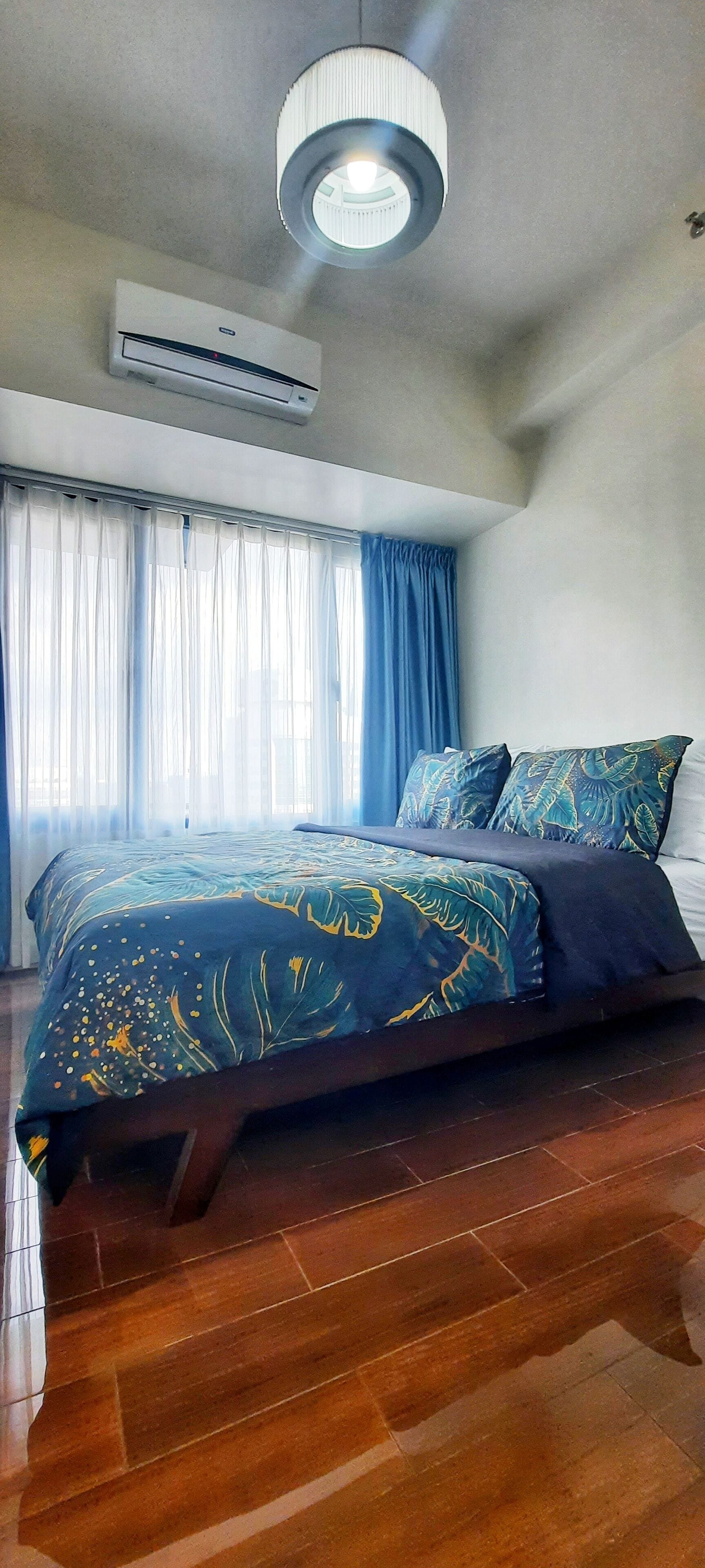A bedroom with a bed, a ceiling light, an air conditioning unit, and a window with curtains.