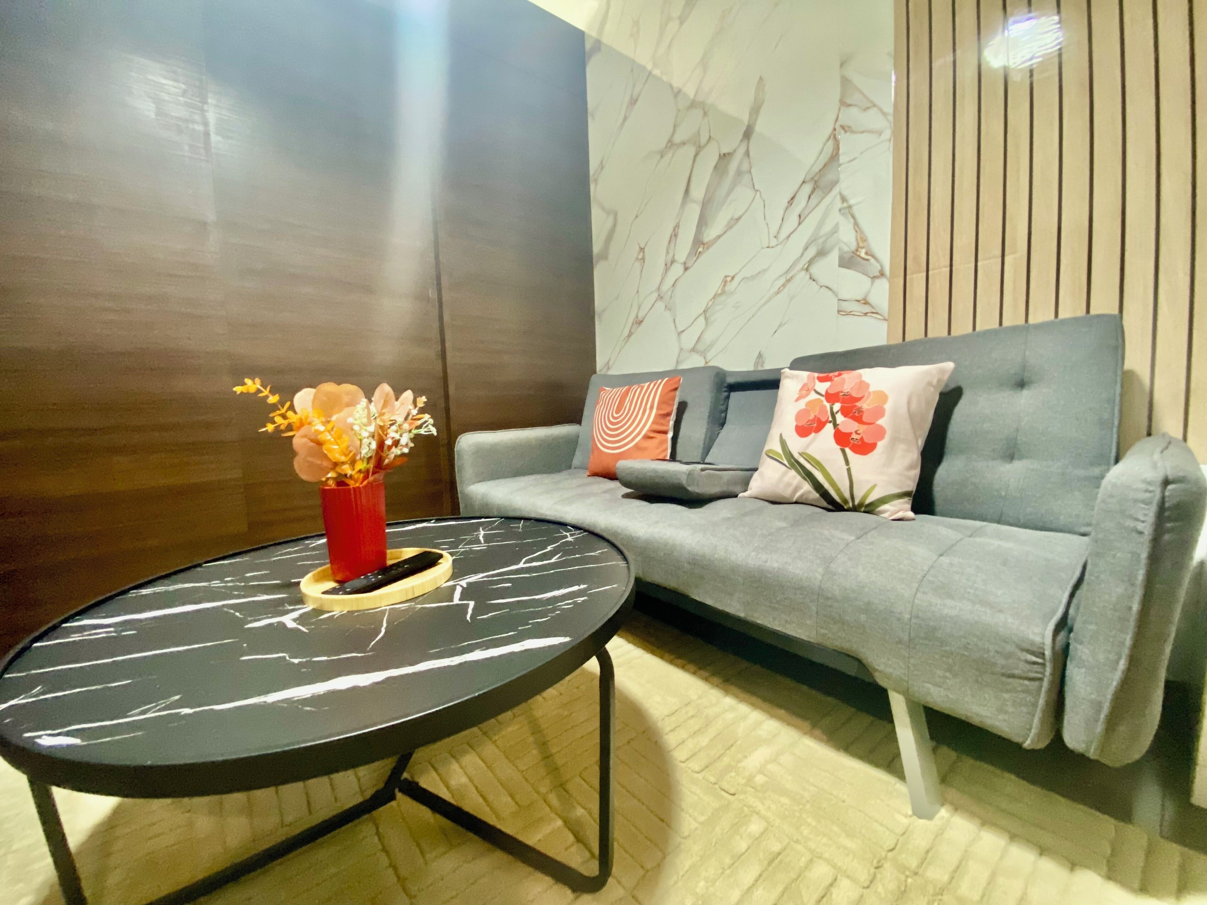 A modern living room with a grey sofa, a black marble coffee table, and a red vase with flowers.