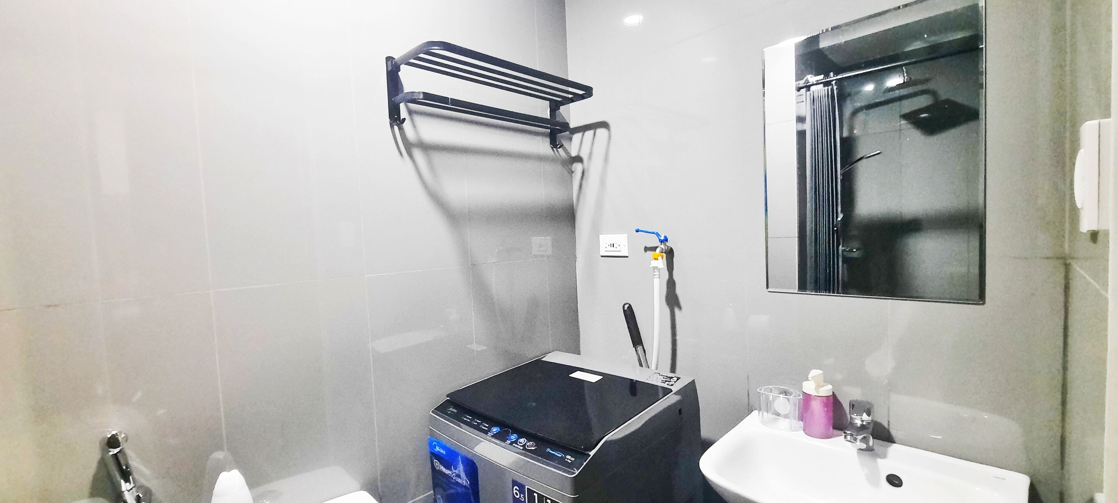 Un baño con un calentador negro, un lavabo blanco, un espejo y un perchero para toallas.
