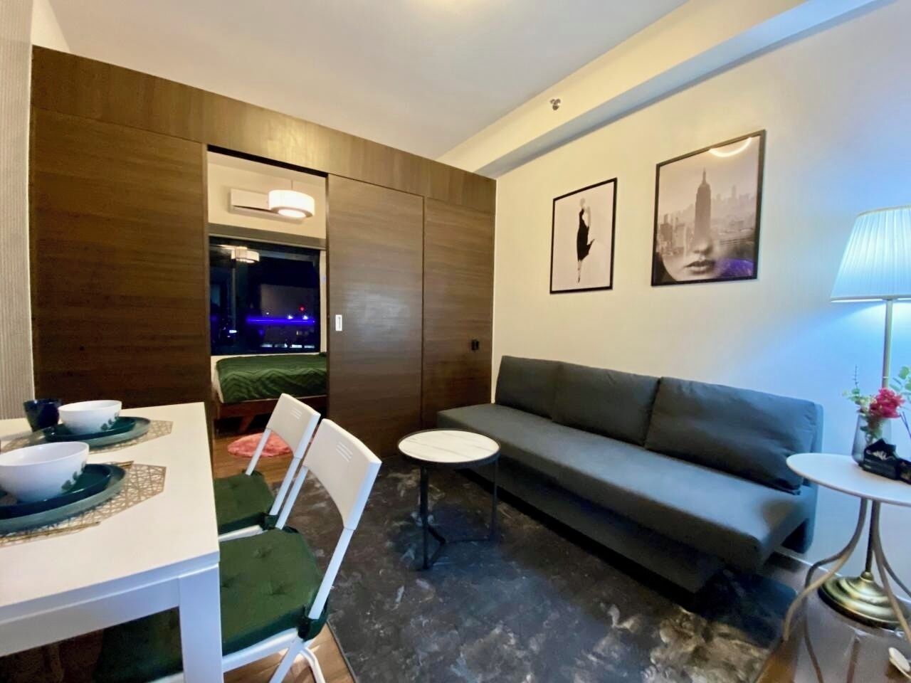Een moderne woonkamer met een bank, een eettafel met stoelen, een klein rond tafeltje en een televisie op de achtergrond.
