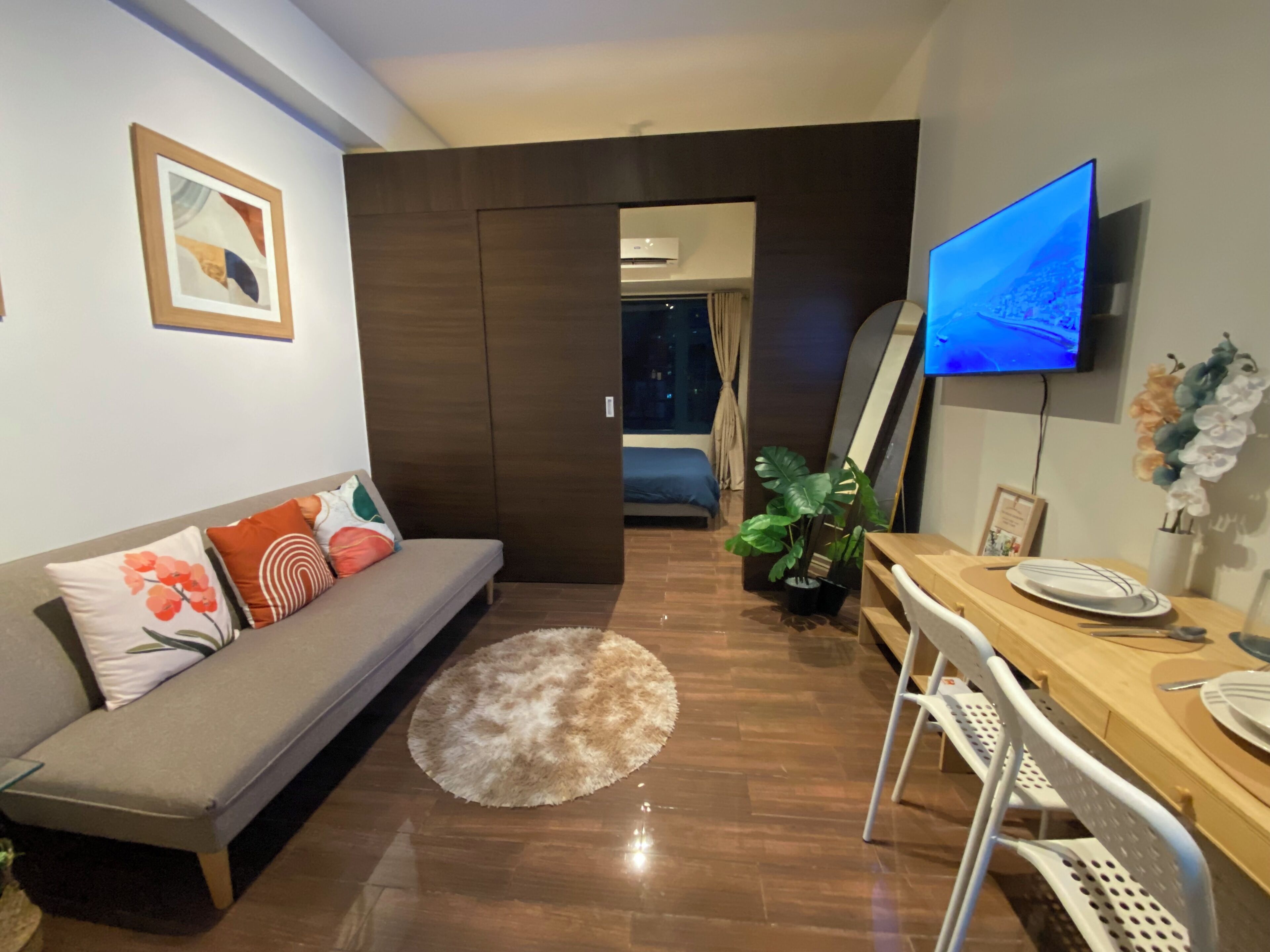 Una sala moderna con un sofá, una mesa de comedor, un televisor y una planta en maceta.