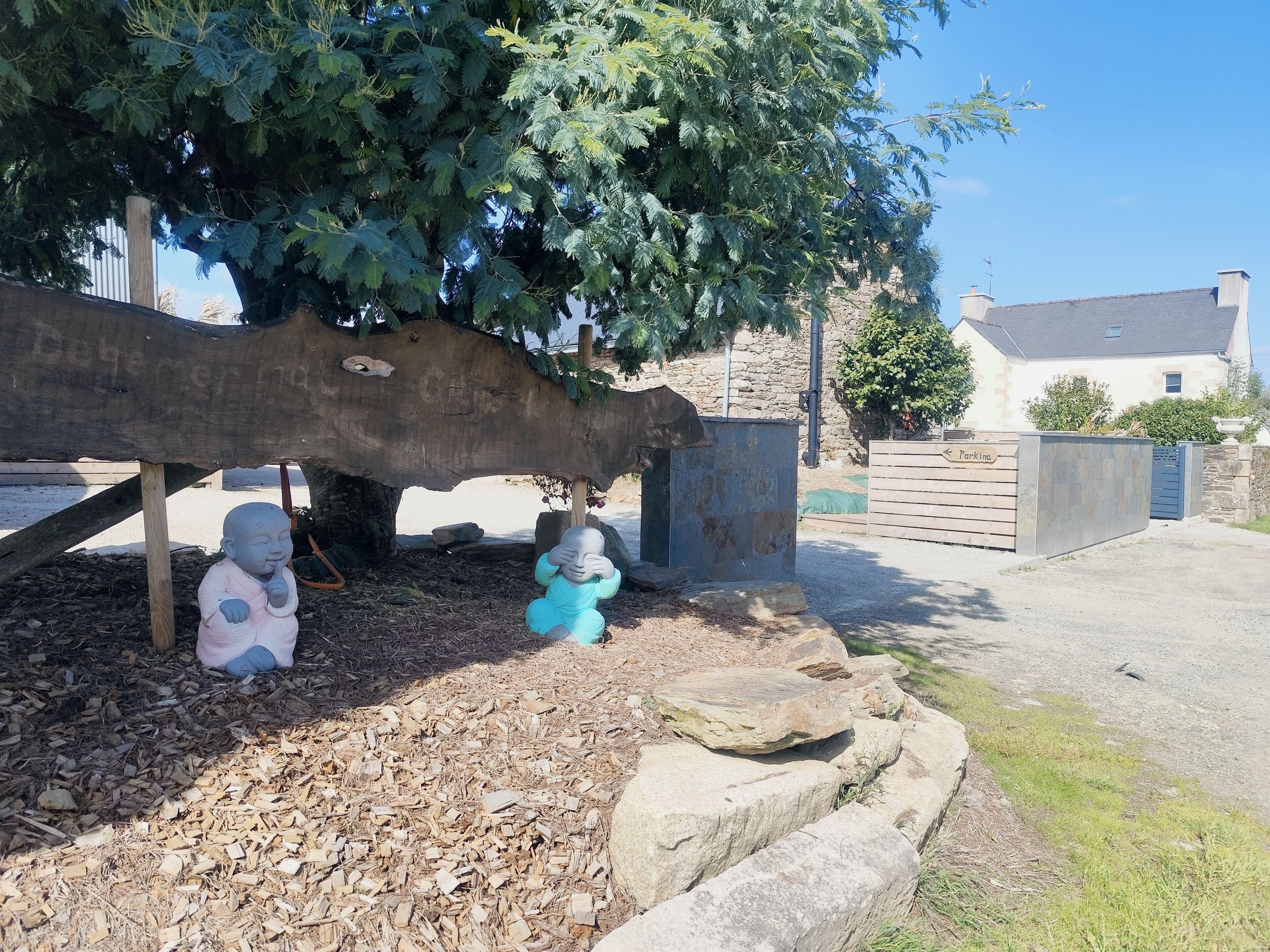 A garden with two statues under a tree, a stone wall, and a building in the background.