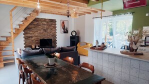 A modern kitchen with a wooden staircase, a stone wall, and a dining area with a large table and chairs.