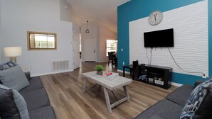 Un salon moderne avec un canapé gris, une table basse en bois et un téléviseur fixé sur un mur à texture.