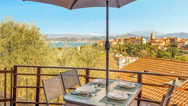 Une table dressée à l’extérieur, offrant une vue sur une ville côtière et sur des montagnes en arrière-plan.