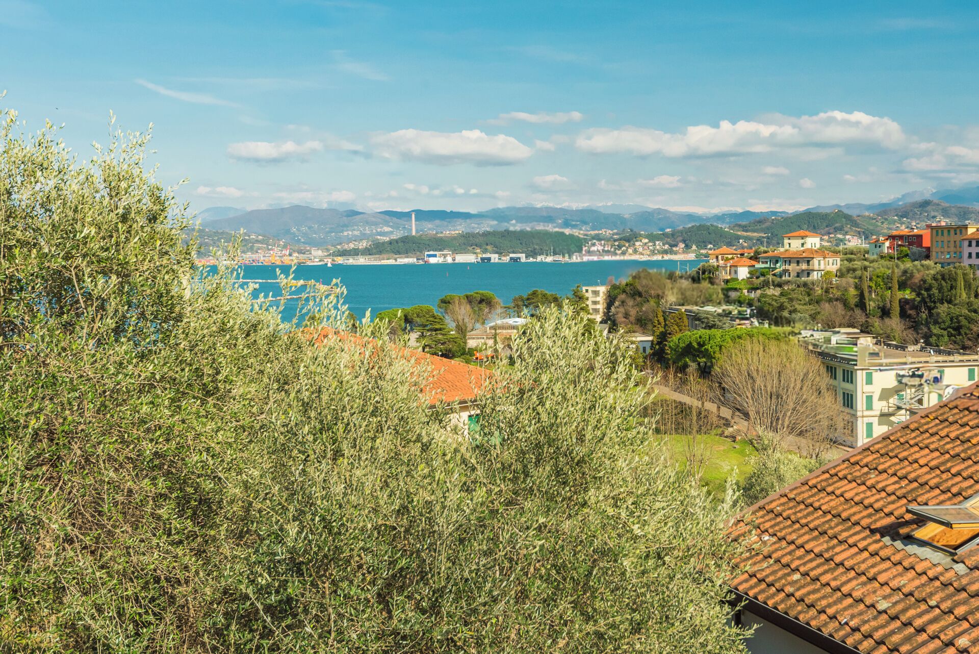 Eine Küstenstadt mit Häusern, blauem Meer und Hügeln im Hintergrund.