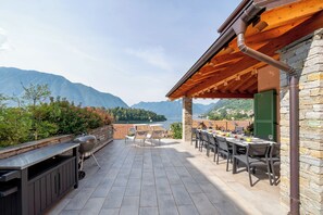 A terrace with a stone wall, a grill, and a table set for dining, overlooking a mountainous landscape. - Villa Comacina, Como Lake (Ossuccio)