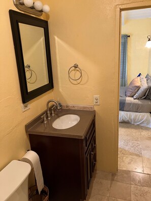 A bathroom with a sink, mirror, towel ring, and a toilet.