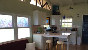 A compact kitchen with white cabinets, a dining area with stools, and a sofa with a cushion. - Bananaquit House (Frederiksted)