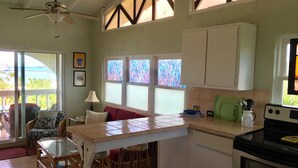 A kitchen with a central island, bar stools, a dining table, and a view of the outdoors. - Bananaquit House (Frederiksted)