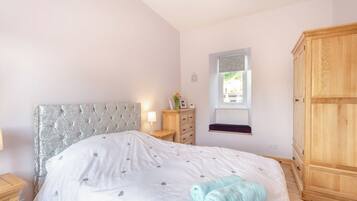 A bedroom with a tufted headboard, a bedside table with a lamp, a window with a view, and a wooden wardrobe.