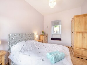 A bedroom with a tufted headboard, a bedside table with a lamp, a window with a view, and a wooden wardrobe. - 1 bedroom accommodation in Pinwherry, near Girvan (Pinwherry, near Girvan)