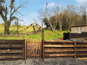 A wooden gate with a curved top, a fenced area with a wooden structure, and a grassy landscape with trees. - 1 bedroom accommodation in Pinwherry, near Girvan (Pinwherry, near Girvan)