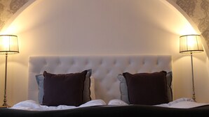 Un dormitorio con cabecera capitonada, dos lámparas de noche y una cama con ropa blanca y dos almohadas.