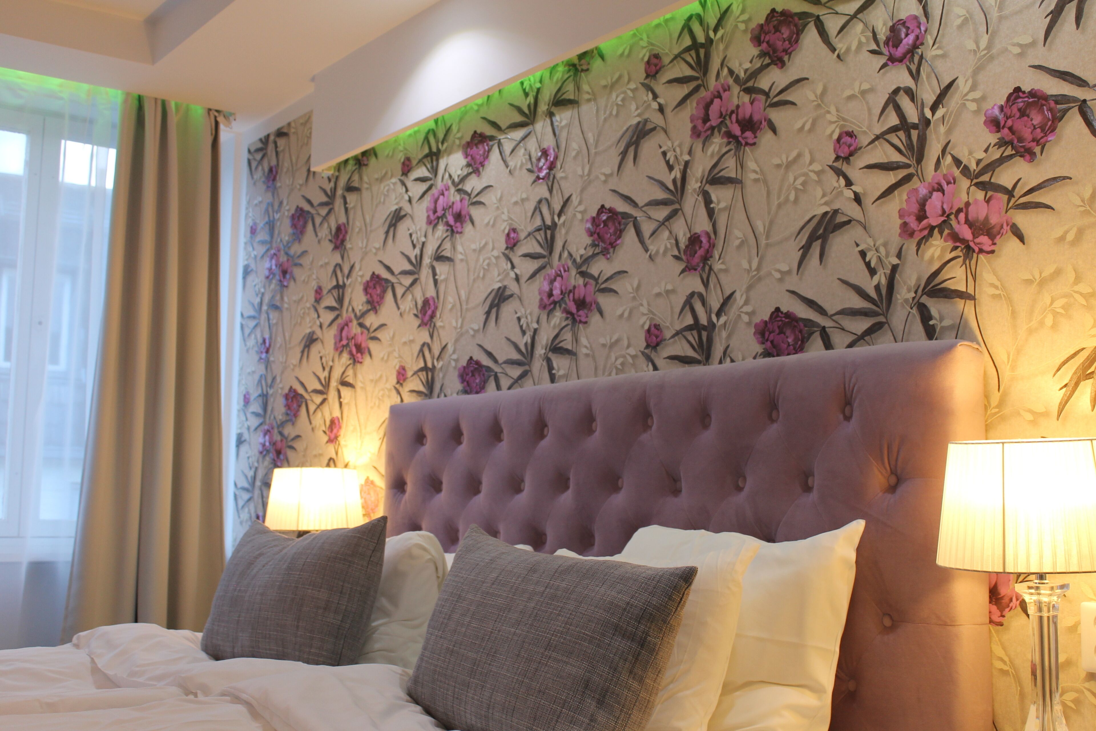 A bedroom with a tufted headboard, two bedside lamps, and floral wallpaper.